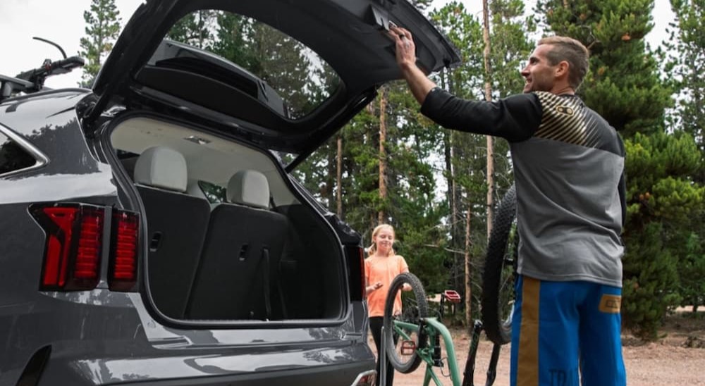 A man opening the hatchback of a grey 2025 Kia Sorento Hybrid.