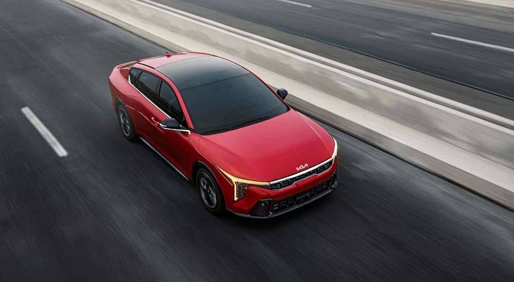 A red 2025 Kia K4 EX driving on a highway.