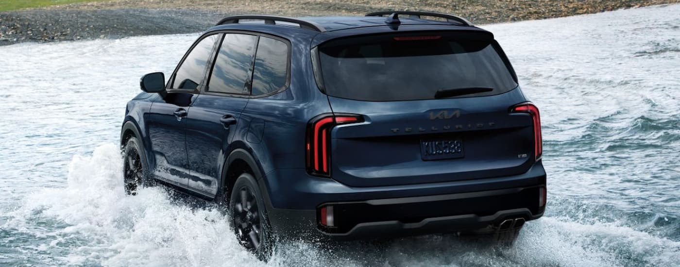 Rear of dark blue 2025 Kia Telluride driving in shallow water.
