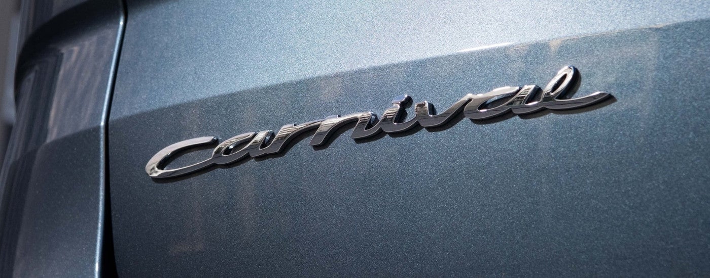 A close up shows the 'Carnival' badge on a grey 2024 Kia Carnival MPV.