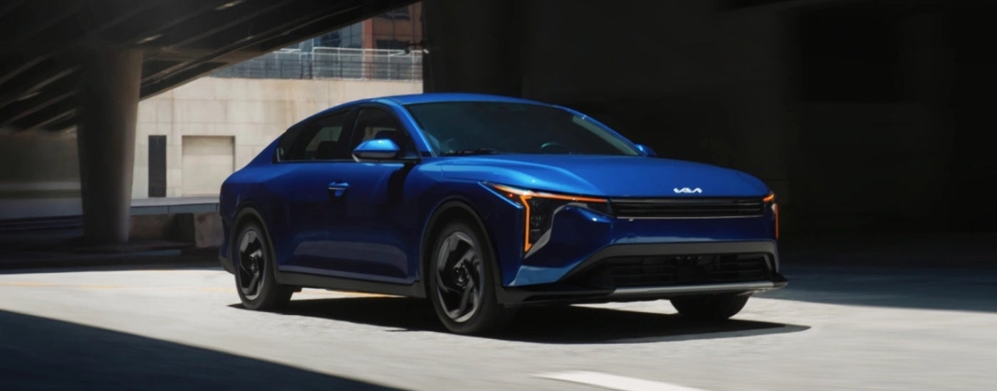 A blue 2025 Kia K4 is shown driving to a Kia dealer near Elmhurst.