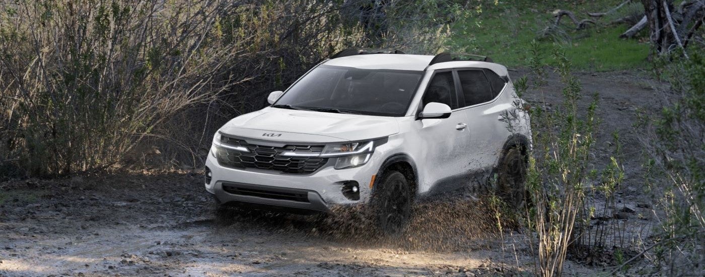 A white 2024 Kia Seltos driving over a muddy trail and angled left.