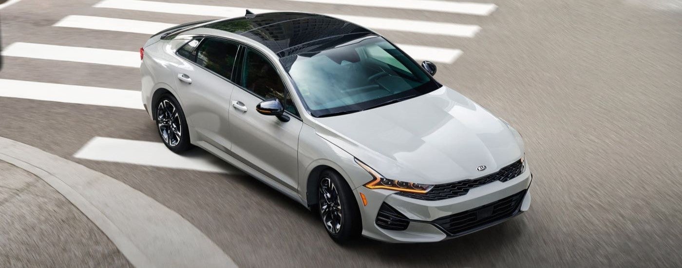 A high angle view of a white 2022 Kia K5 driving through an intersection.