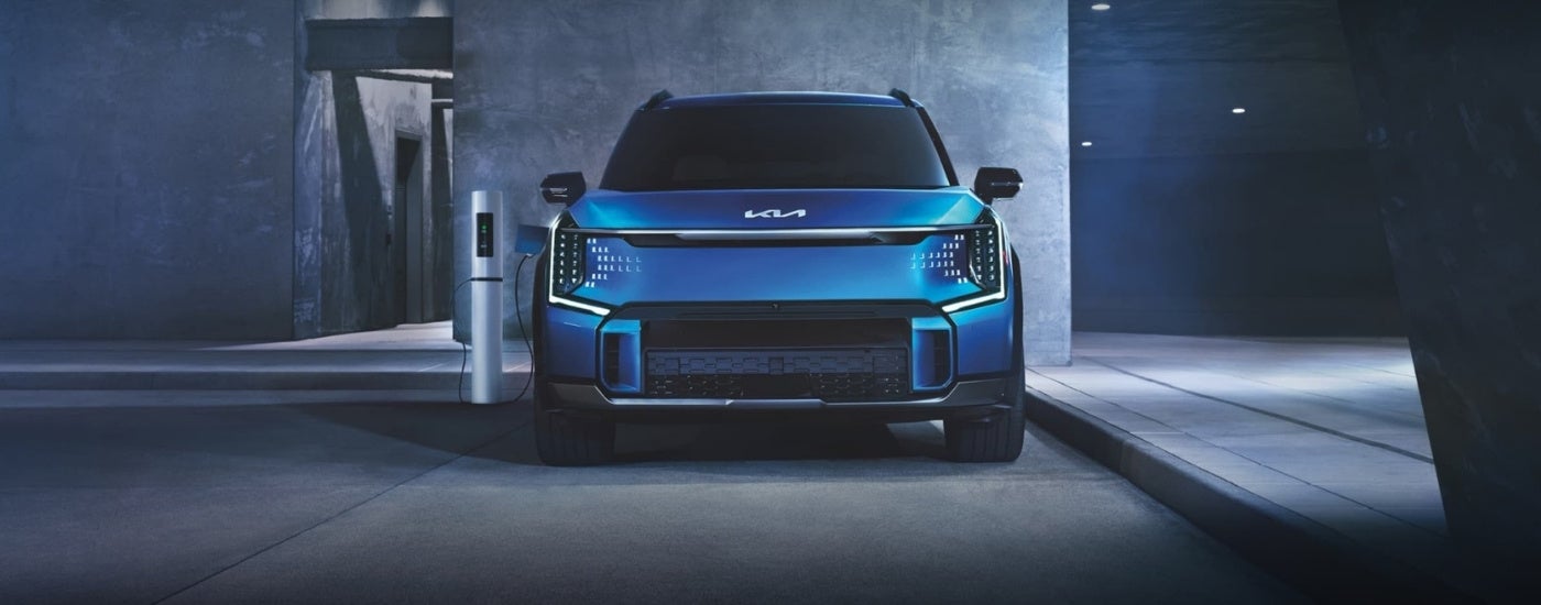 Front angle view of a blue 2024 Kia EV9 parked at a charging station.